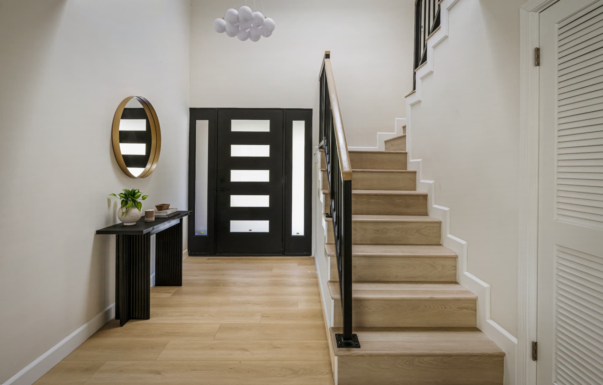 Entry foyer with wood stair, round brass mirror and cluster pendant